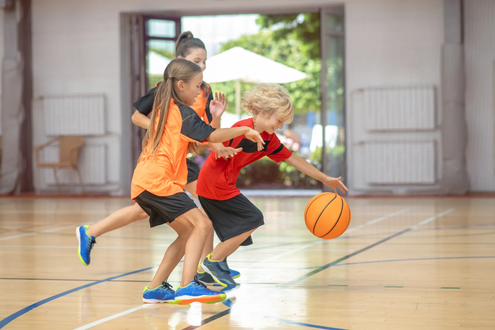 Children playing basketball together on an indoor court.